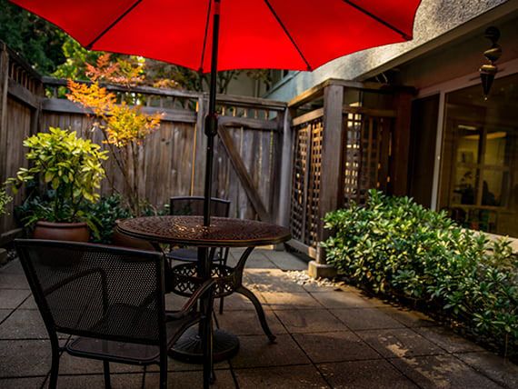 A cozy patio with a red umbrella, surrounded by lush greenery.