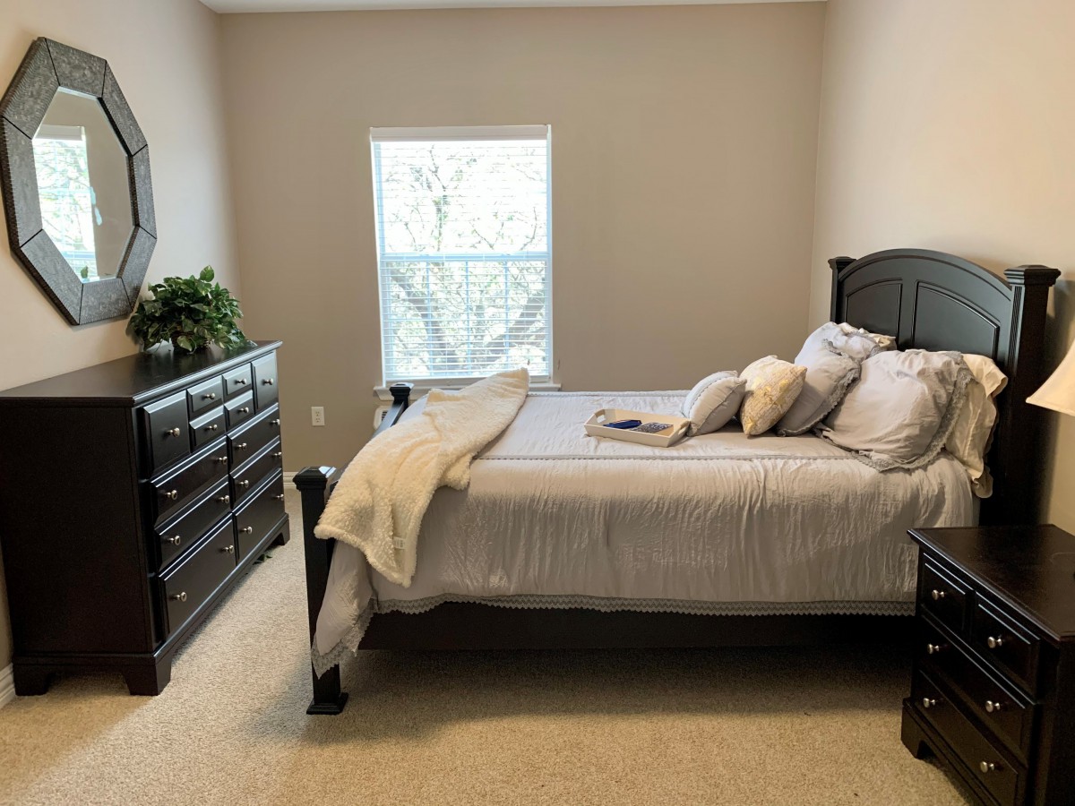 A cozy bedroom with a neatly made bed and dark wooden furniture.