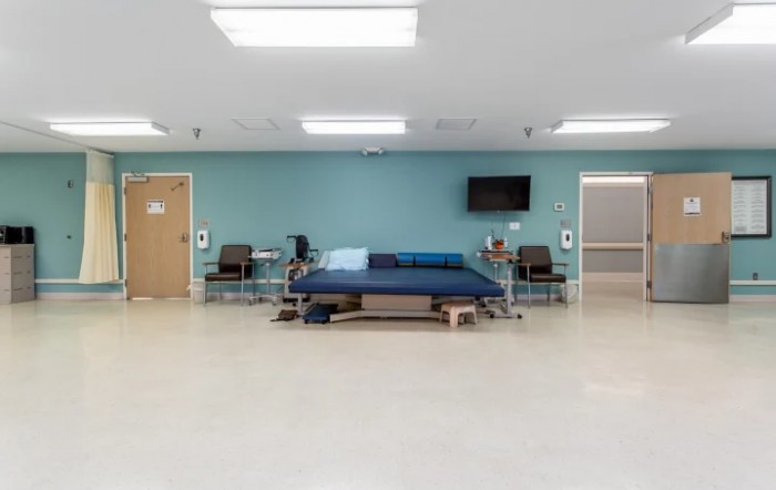 An empty hospital patient room with a bed and chairs.