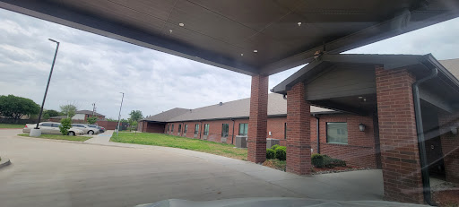 A view of a brick residential building with a covered entrance, set against a cloudy sky.