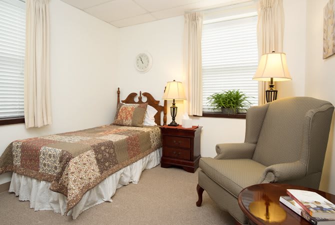 A cozy bedroom with a single bed, nightstand, and armchair by the window.