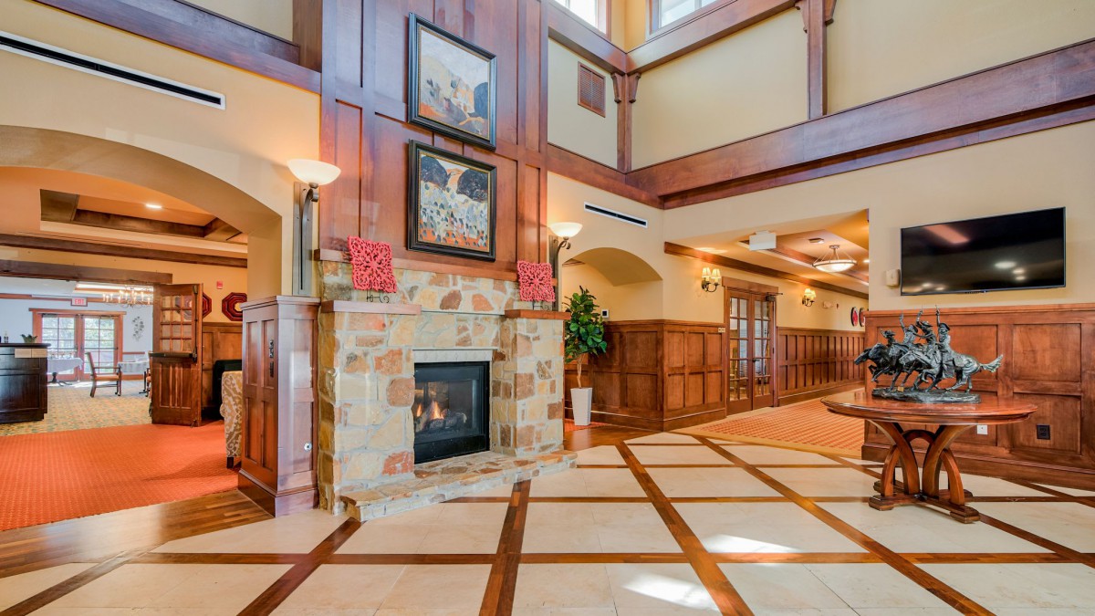 A spacious lobby area featuring a fireplace with stone surround, wooden paneling, and high ceilings.