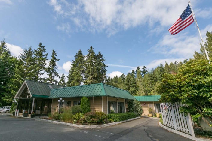 A building with a green roof surrounded by trees and a clear blue sky, featuring an American flag near the entrance.