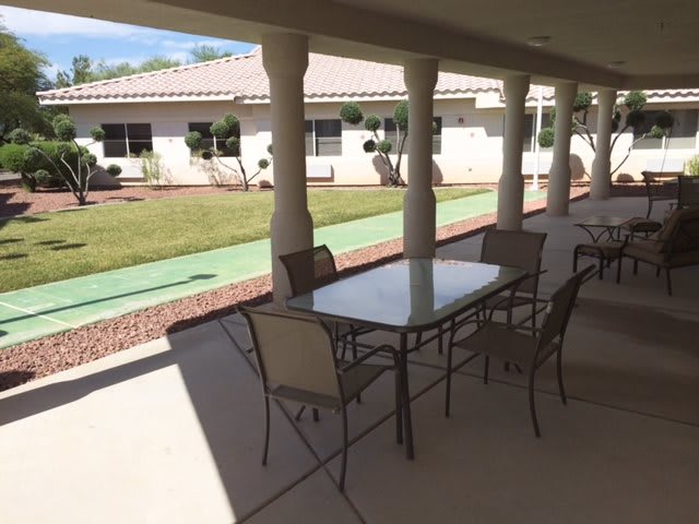 A covered outdoor patio area with a table and chairs, overlooking a garden.