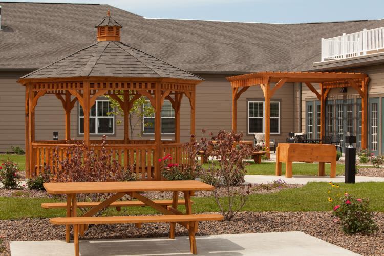 A serene backyard featuring a wooden gazebo, pergola, and picnic table surrounded by well-maintained landscaping.