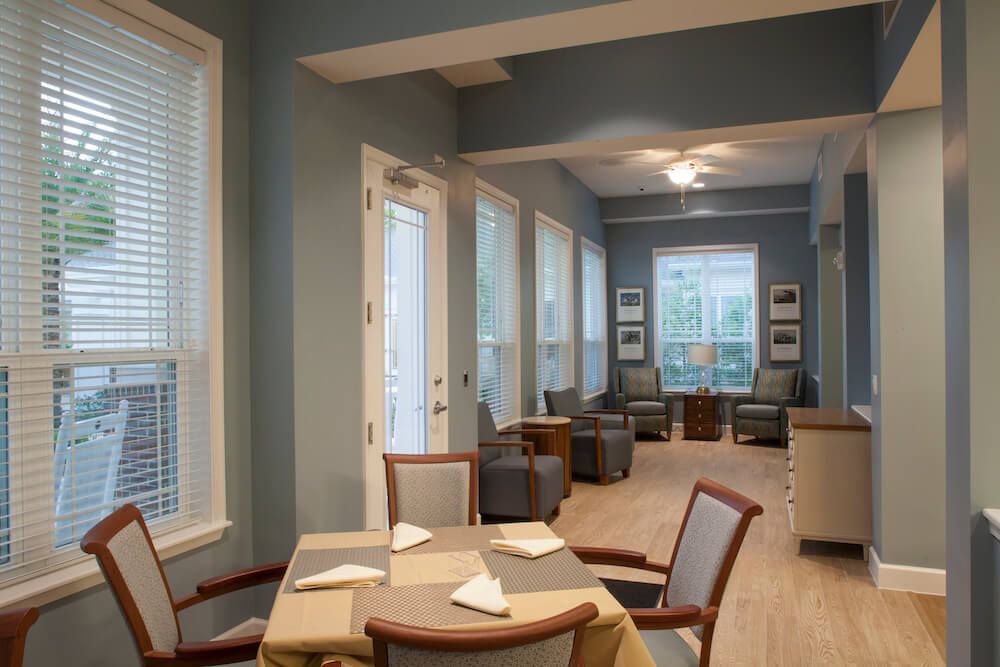 A modern dining area with tables and chairs, lit by natural light through large windows.