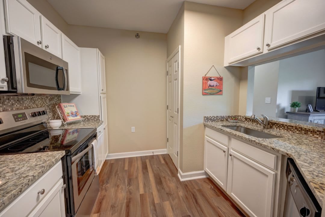 A modern kitchen with white cabinets, stainless steel appliances, and wood flooring.