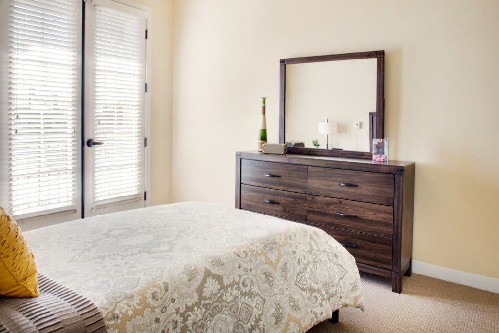 A neatly arranged bedroom featuring a bed and a dresser with a mirror.