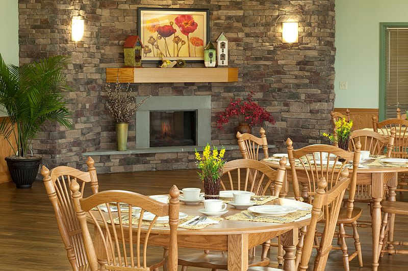 A cozy dining room with a brick fireplace, decorated with wooden furniture and a floral painting.