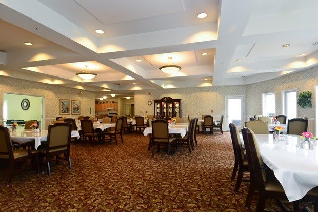 A well-lit dining room with neatly arranged tables and chairs, featuring a patterned carpet and elegant lighting fixtures.