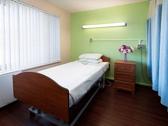 A simple hospital room with a single bed and green walls.