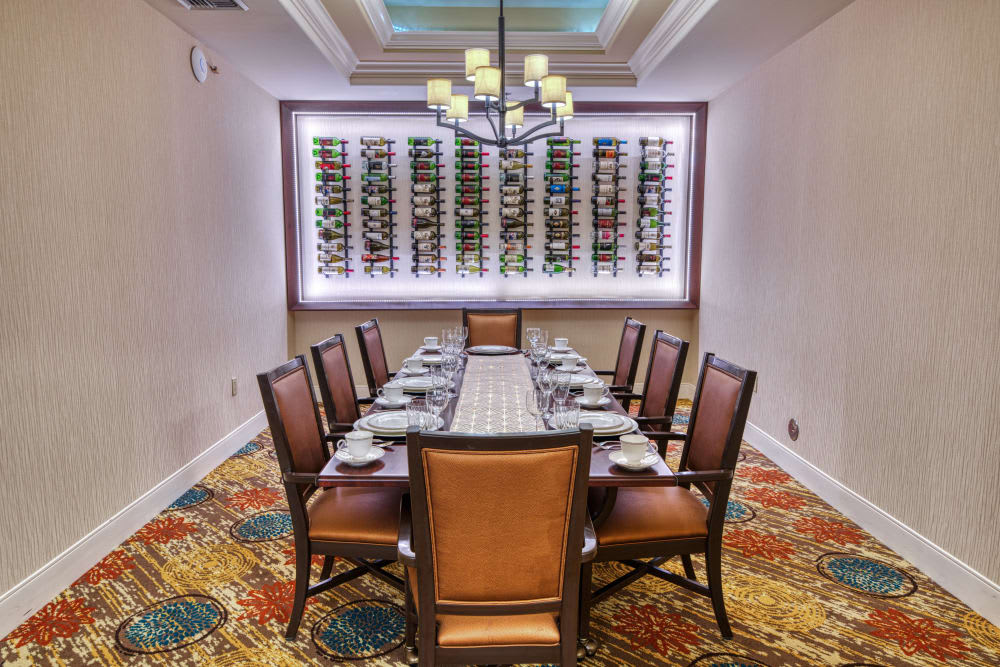 An elegant dining room with a long table, surrounded by chairs and featuring a wine rack on the wall.
