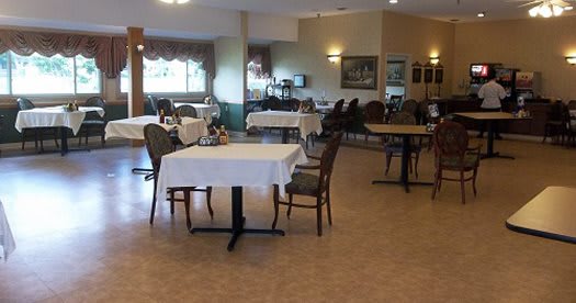 An empty dining area with neatly arranged tables and chairs, each table covered with a white tablecloth.