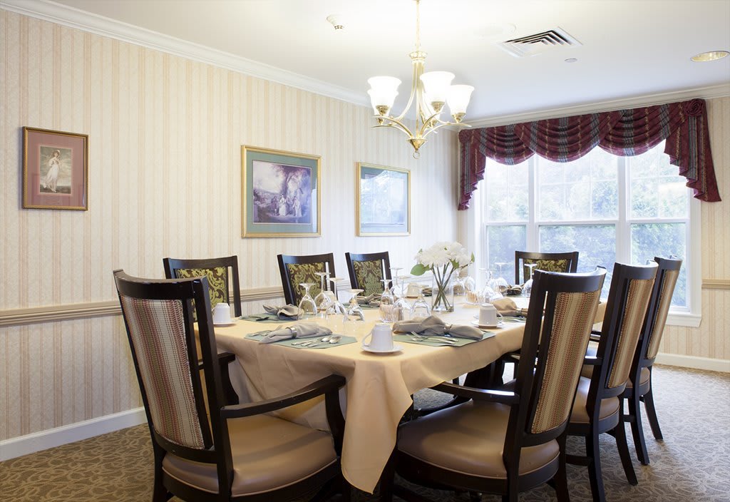 An elegantly set dining room table with a chandelier overhead and framed artwork on the walls.