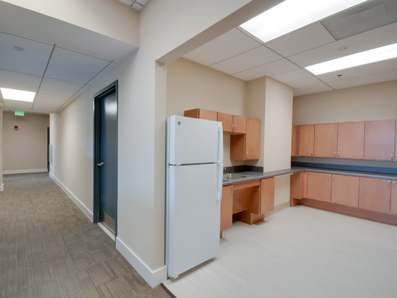 A compact office kitchen area with a refrigerator and wooden cabinets.