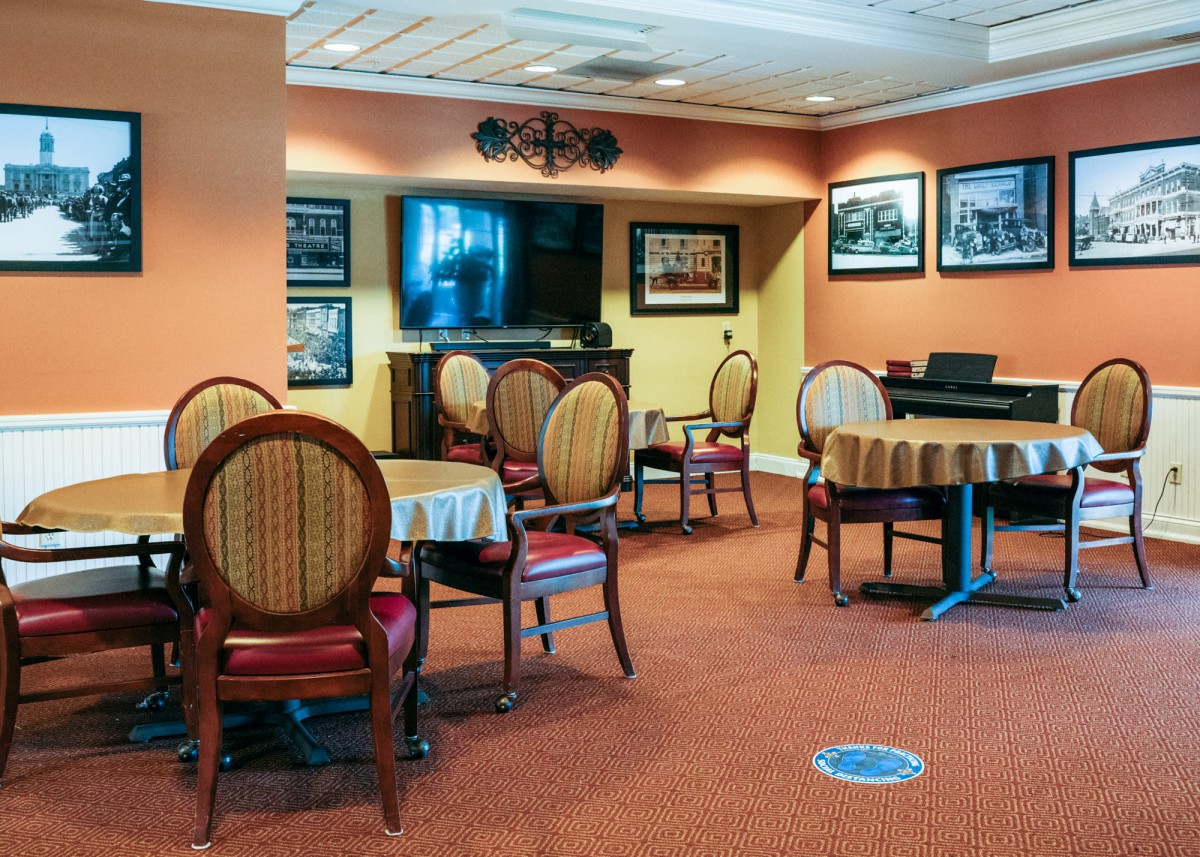 A cozy dining area with round tables and elegant chairs set on a carpeted floor, decorated with wall art.