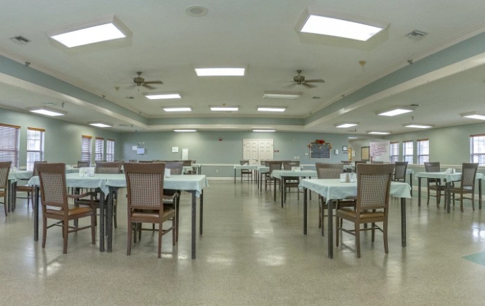 A spacious dining room with neatly arranged tables and chairs under bright ceiling lights.