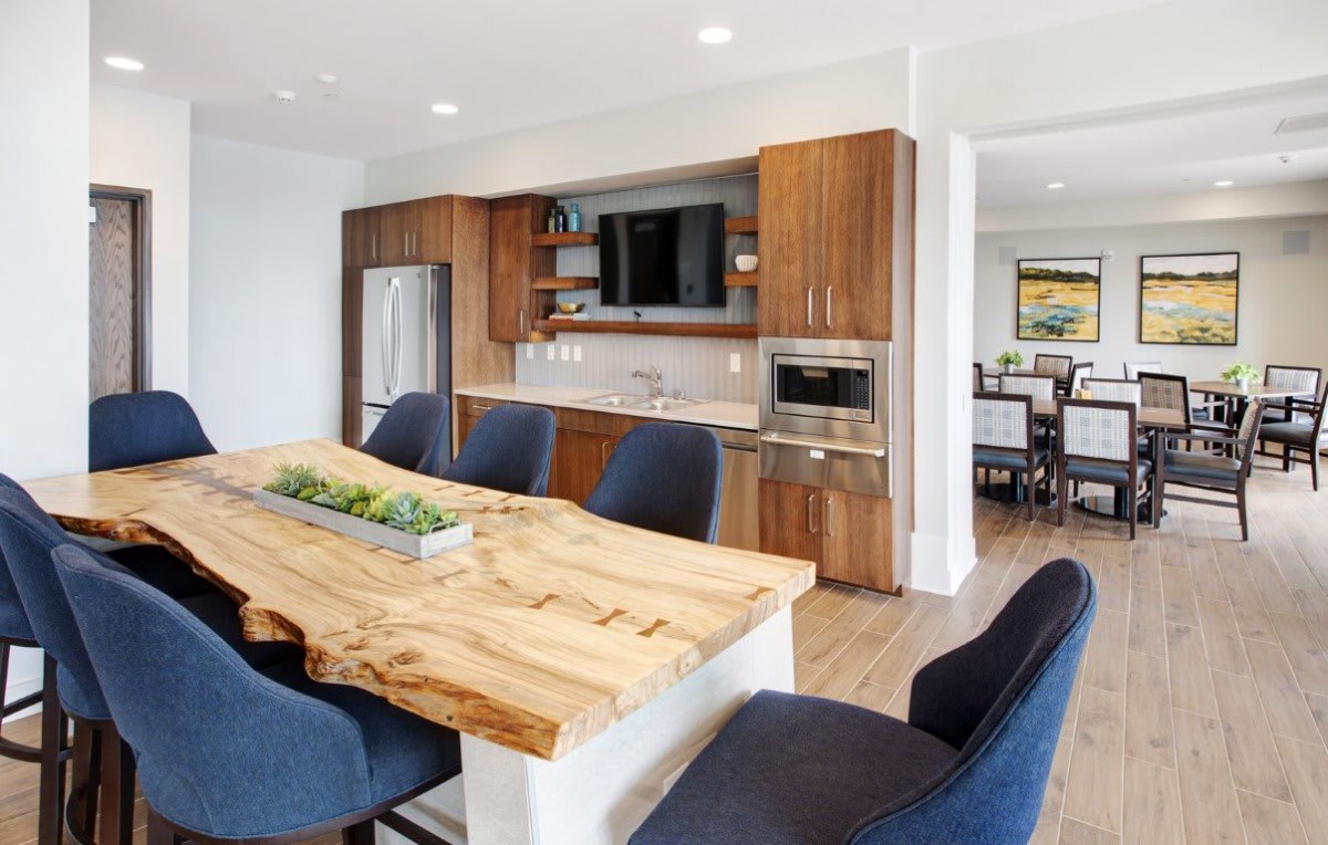 A modern kitchen and dining area with a wooden table, dark chairs, and stainless steel appliances.