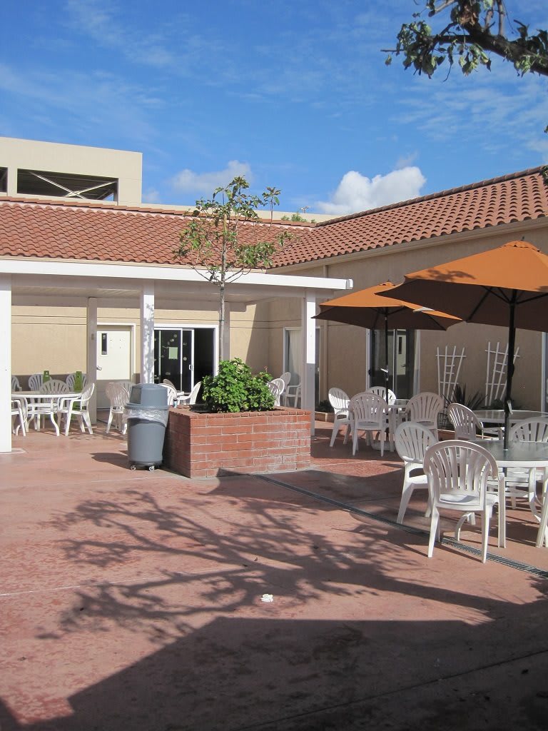An outdoor patio area with chairs, tables, and umbrellas under a clear blue sky.