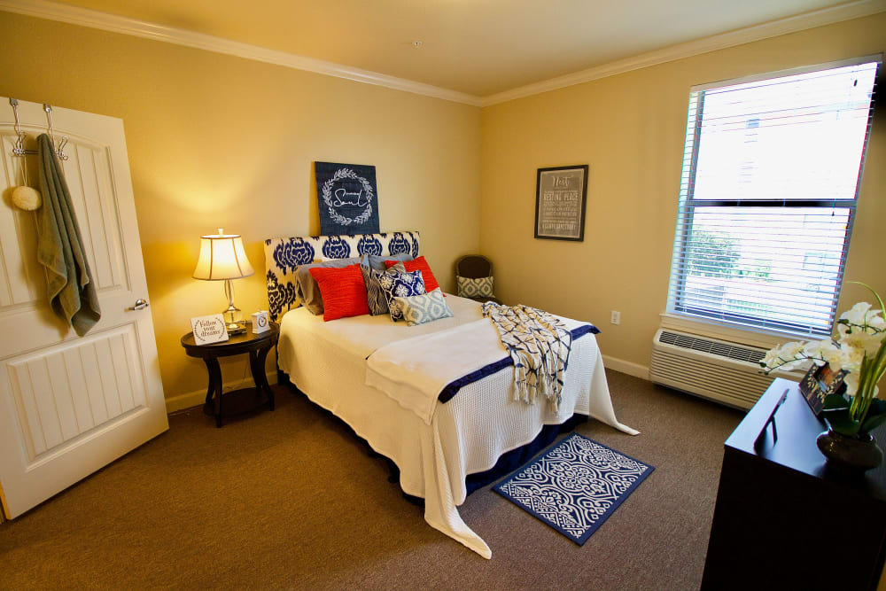 A cozy bedroom with a neatly made bed, decorative pillows, and a warm lamp lighting the room.