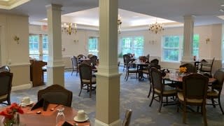 A spacious dining room with multiple tables and chairs, featuring chandeliers and large windows.