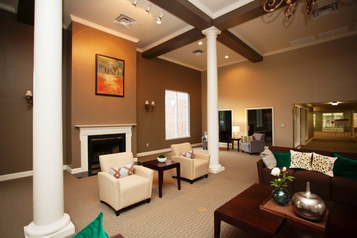 A spacious living room with a fireplace, armchairs, and a coffee table, featuring high ceilings and decorative pillars.