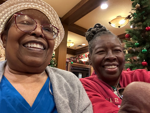 Two joyful women smiling together in a cozy setting decorated for the holidays.
