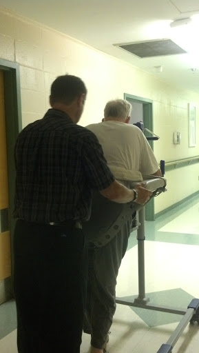 A caregiver assisting an elderly person with a walking aid in a healthcare facility.