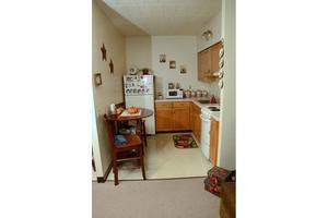 A cozy, compact kitchen area in an apartment with a small dining table, refrigerator, microwave, and wooden cabinets.