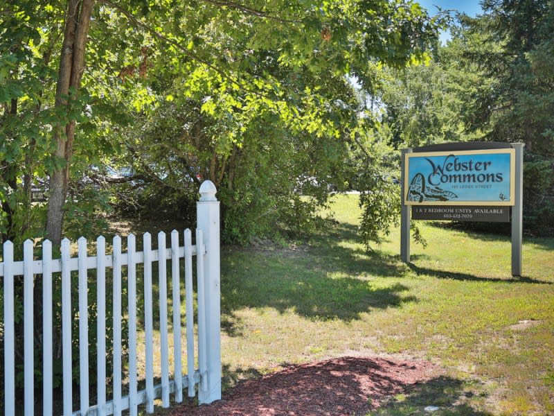 A wooden sign along a white picket fence in a lush, green garden setting.