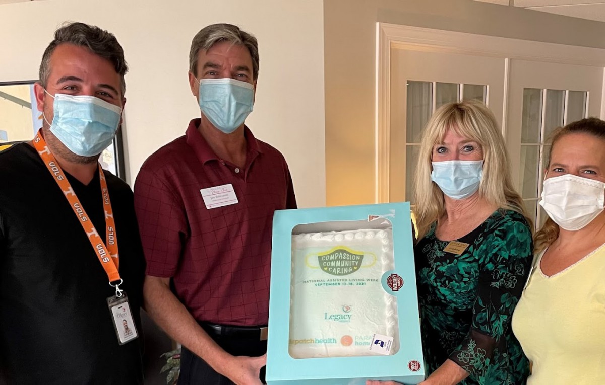 Three people wearing masks hold a boxed certificate indoors.