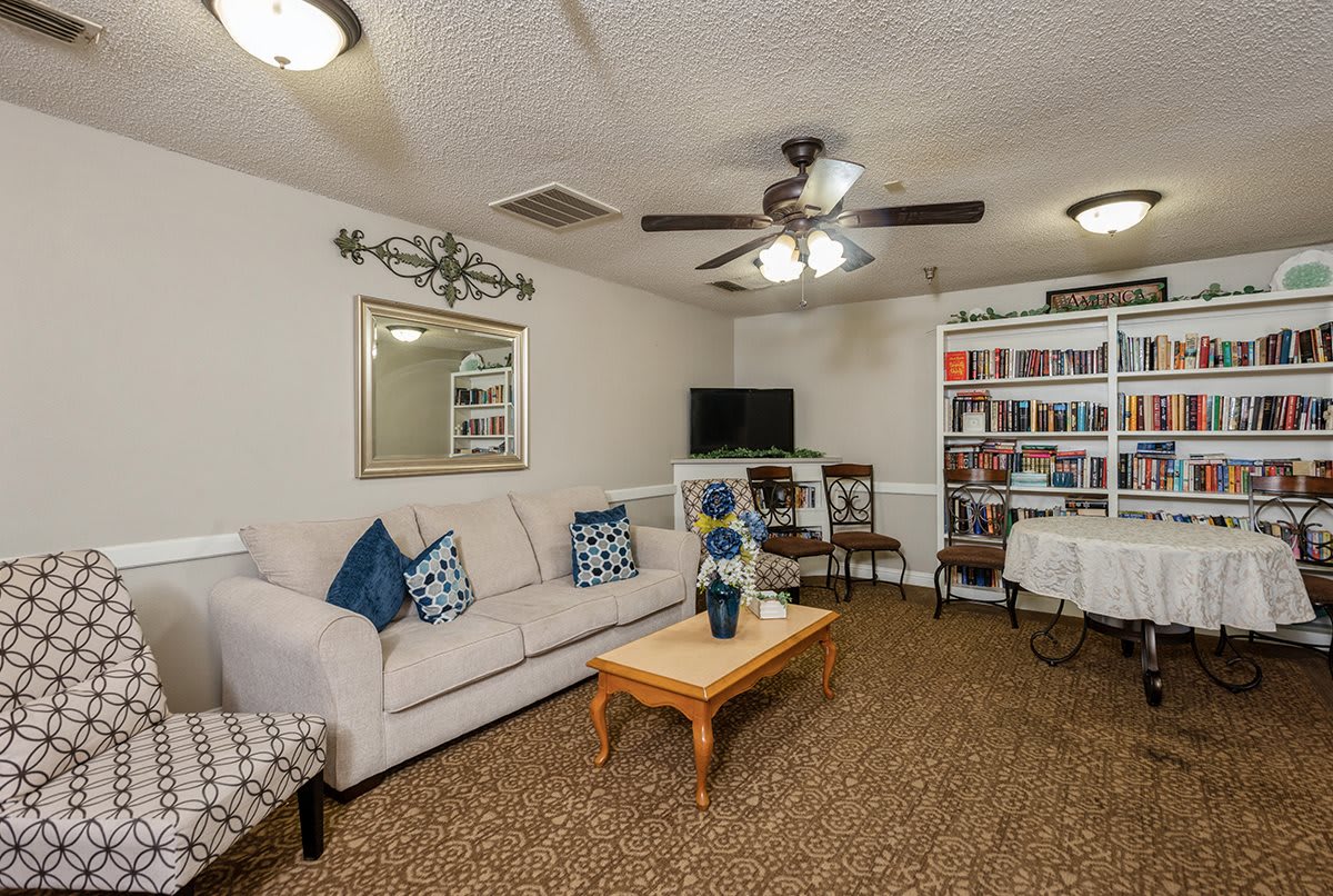 A cozy living room with a sofa, coffee table, and bookshelf under ceiling fans.