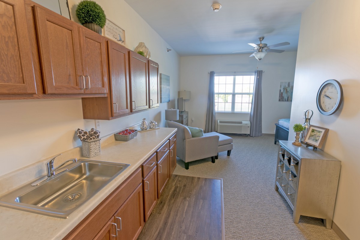 A modern apartment interior featuring a kitchen open to a cozy living area with natural light from a large window.