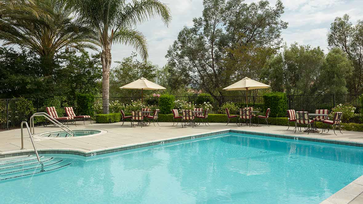 A tranquil outdoor swimming pool area with palm trees and patio seating.