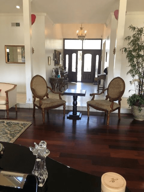 A cozy living room with elegant chairs and a small table, featuring hardwood floors and a chandelier near the entrance.