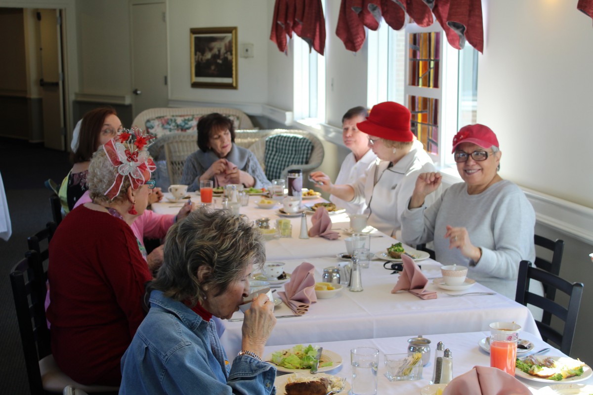 A group of people enjoying a meal together indoors, many wearing decorative hats.