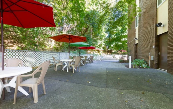 A serene outdoor patio area with tables, chairs, and umbrellas surrounded by greenery.