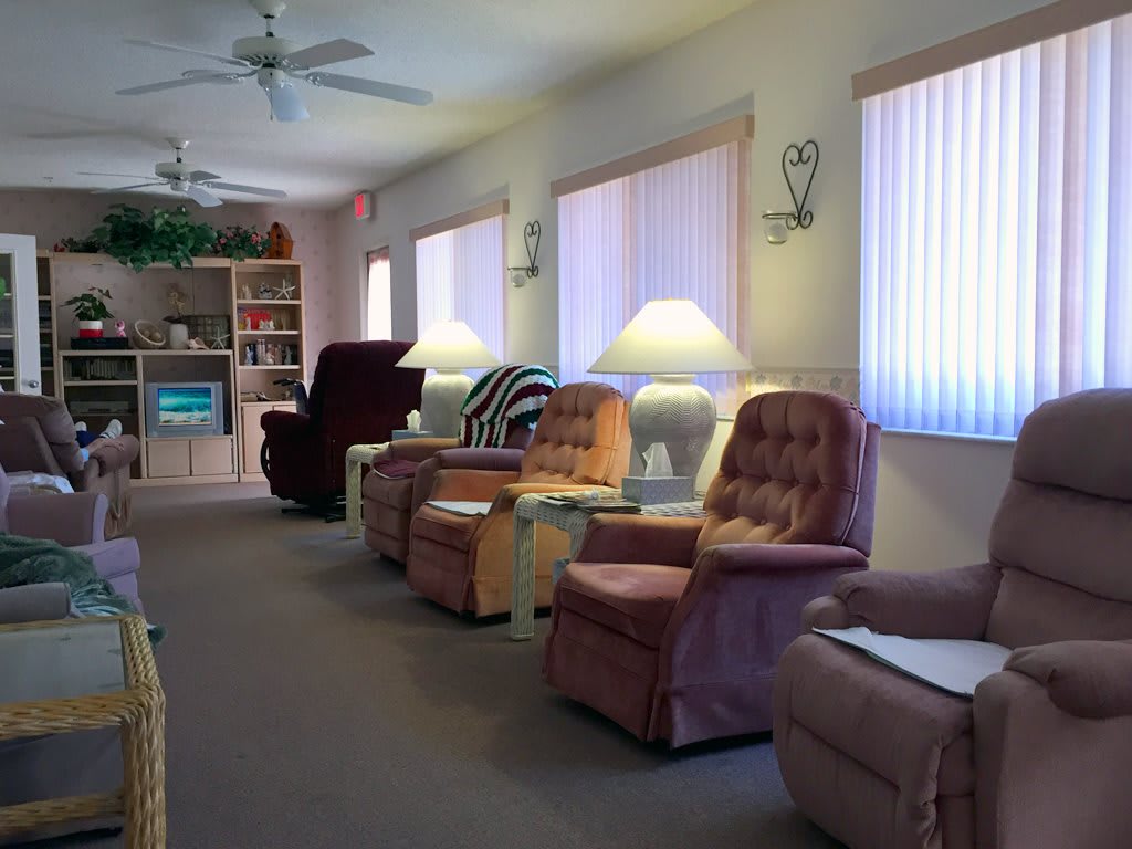 A cozy living room with a row of armchairs, side tables with lamps, and sunlight filtering through vertical blinds.