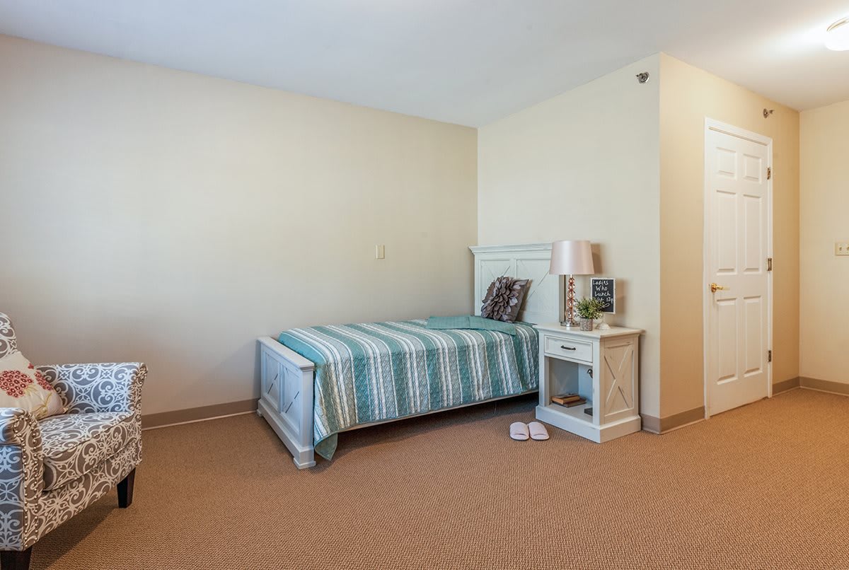 A minimalist bedroom featuring a single bed with striped bedding, alongside a nightstand and lamp.