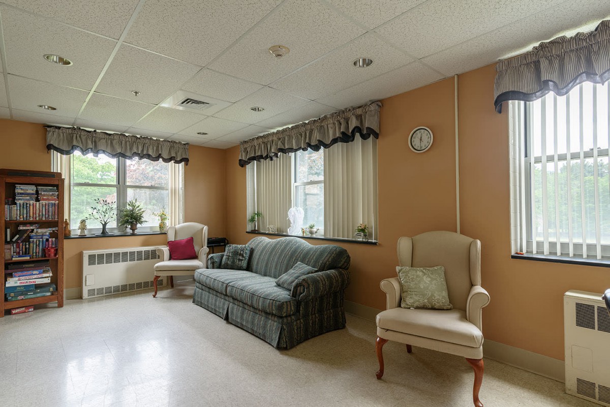 A cozy living room with a sofa, armchair, and windows adorned with curtains.