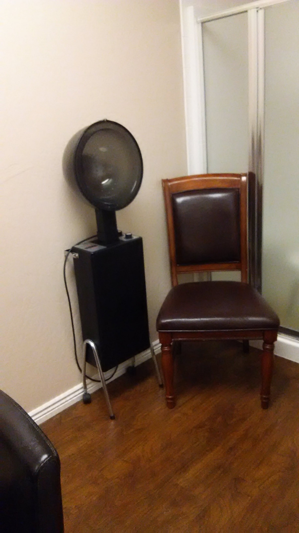 A salon hair dryer next to a wooden chair in a corner.
