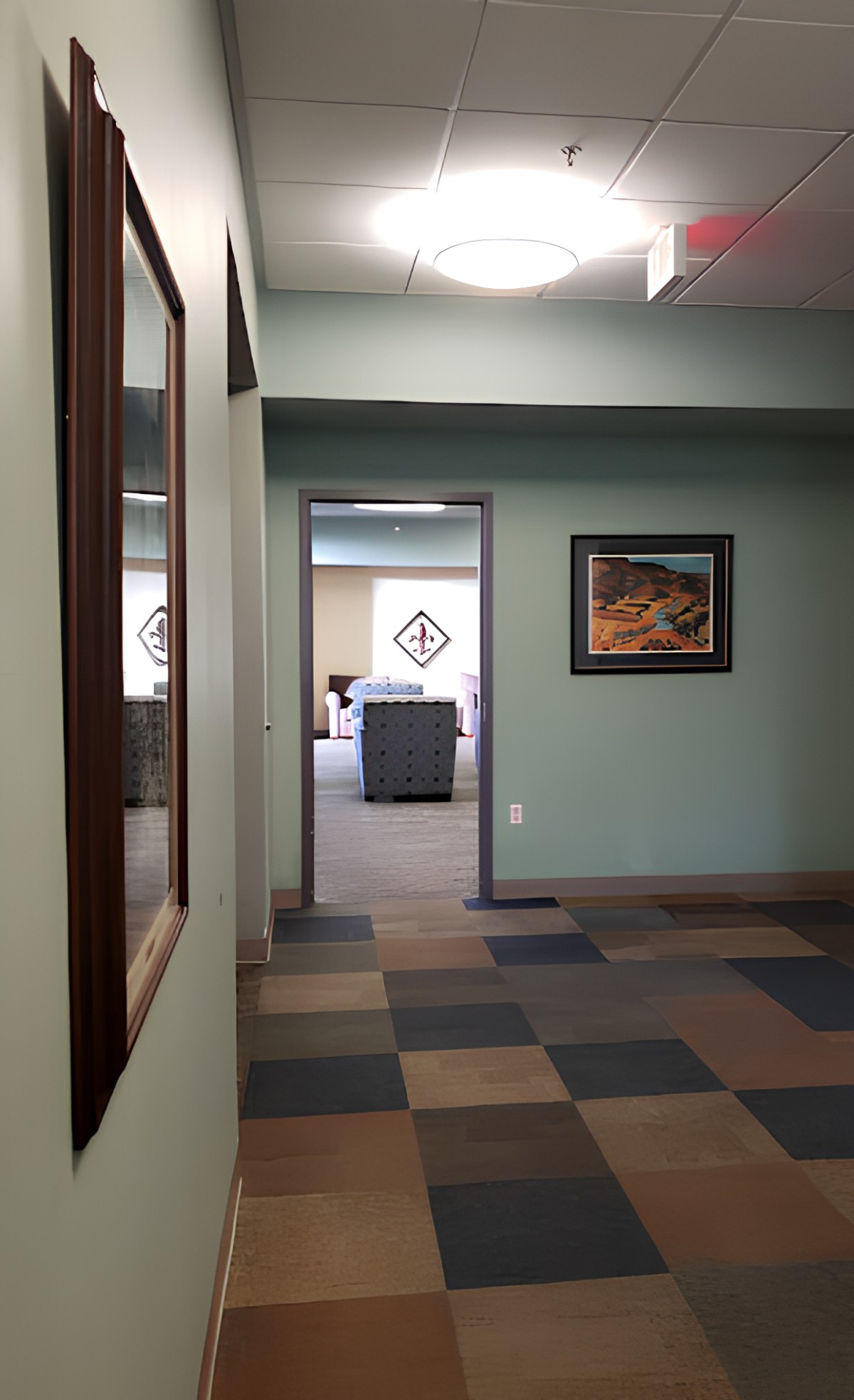 A view down a hallway in an office with artwork on the walls and patterned flooring.