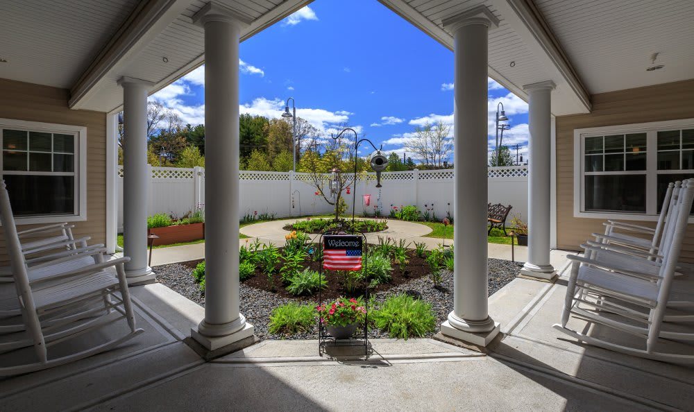 A beautifully landscaped garden viewed from a covered patio with large columns and a bright blue sky overhead.