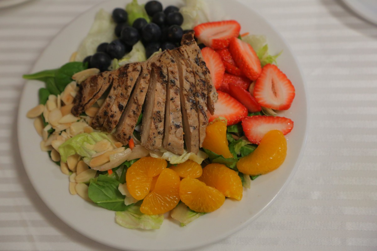 A colorful salad with grilled chicken, strawberries, oranges, blueberries, and lettuce.