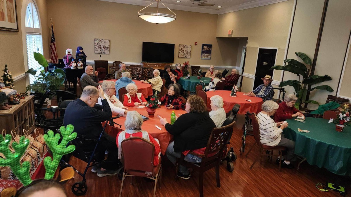 A group of seniors gathered indoors around tables for a community event.