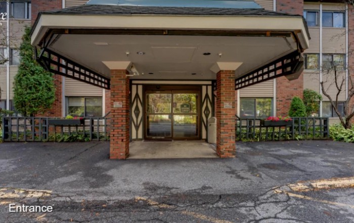 Entrance of a building with brick pillars and glass doors, surrounded by plants.