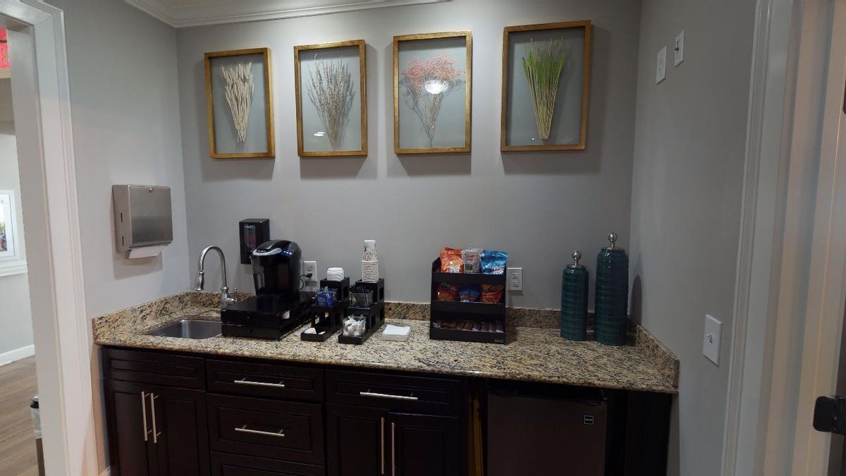 A neatly arranged coffee station with a coffee maker, snacks, and decorative artwork on the wall.