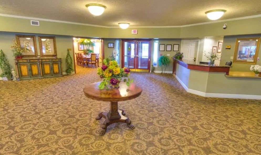 A hotel lobby with a central table adorned with flowers, surrounded by elegant carpeting and warm lighting.