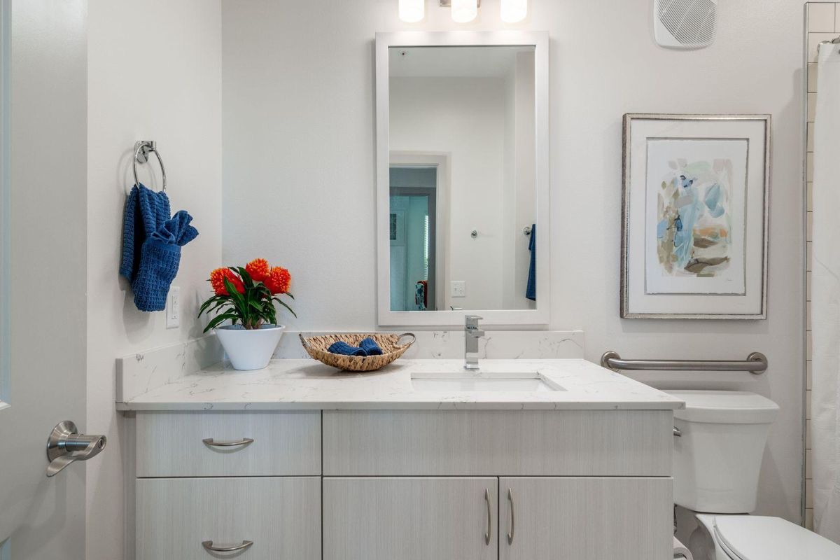 A modern bathroom with a sleek white countertop, adorned with a bowl of red flowers and a wicker basket for toiletries.