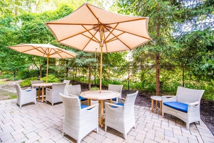 A serene outdoor patio setting with tables, chairs, and large umbrellas surrounded by lush greenery.